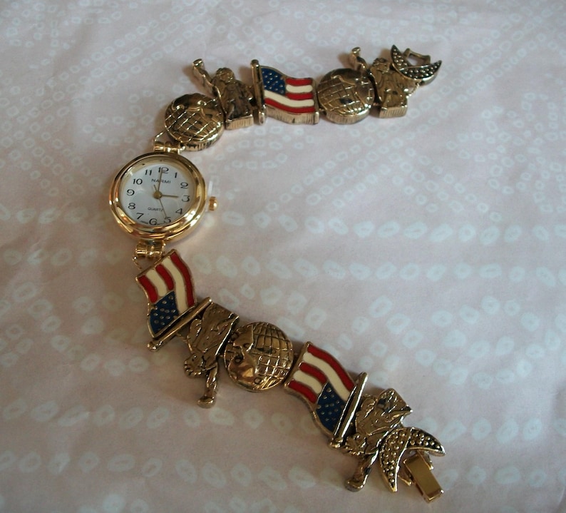 May include: A gold-tone watch bracelet with a white face and black hands. The bracelet features a repeating pattern of American flags, globes, and stars.