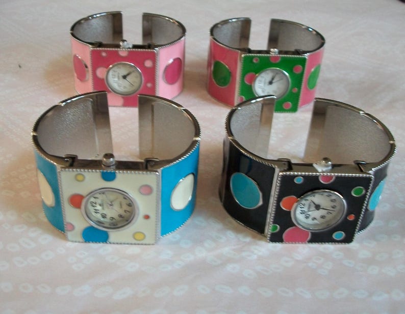 May include: Four silver bangle bracelets with colorful enamel and polka dot designs. Each bracelet features a square watch face with a white background and black hands.