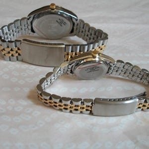 May include: Two silver and gold tone wristwatches with metal bands. The watches have round faces and are both set to the same time.