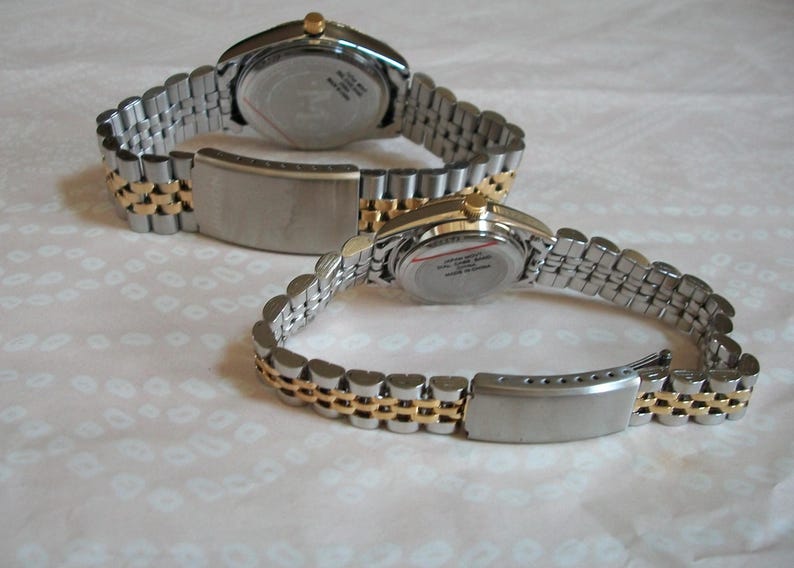 May include: Two silver and gold tone wristwatches with metal bands. The watches have round faces and are both set to the same time.