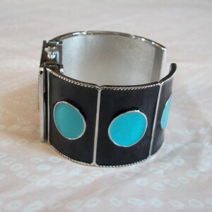 May include: A silver bangle bracelet with black enamel and turquoise blue circles. The bracelet is hinged and has a silver clasp.