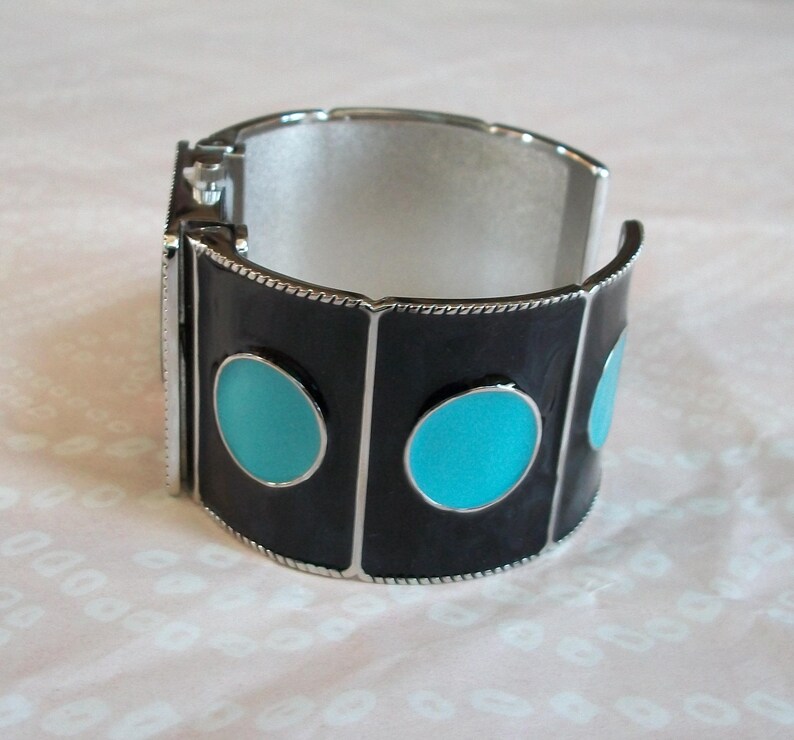 May include: A silver bangle bracelet with black enamel and turquoise blue circles. The bracelet is hinged and has a silver clasp.