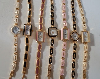 May include: Seven gold-tone wristwatches with different coloured bands. The bands are white, black, pink, and black and white. The watches have square and round faces.