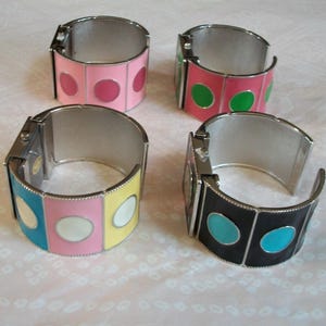 May include: Four silver bangle bracelets with colorful enamel circles. The bracelets have a hinged design and are decorated with different colored circles.