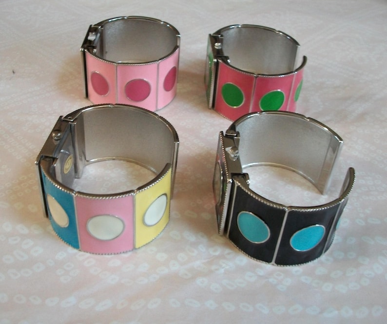 May include: Four silver bangle bracelets with colorful enamel circles. The bracelets have a hinged design and are decorated with different colored circles.