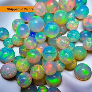 May include: A collection of iridescent opal spheres in various sizes. The opals display a range of colours, including blue, green, yellow, and red, with a milky white base. The spheres are scattered across a white surface.