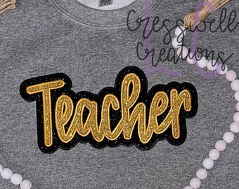 May include: A gray sweatshirt with the word "Teacher" in gold glitter letters with a black outline. The letters are in a cursive font.