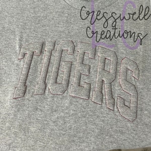 May include: Gray t-shirt with the word "TIGERS" embroidered in white with red stitching.