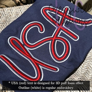 May include: Navy blue fabric with a red "USA" design in a 3D puff foam effect, outlined in white embroidery. The design is centered on the fabric. The text at the bottom of the image says "USA (red) text is designed for 3D puff foam effect Outline (white) is regular embroidery."