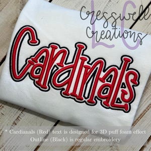 May include: White fabric with the word "Cardinals" embroidered in red with a black outline. The text is designed for a 3D puff foam effect. "Cresswell Creations" is written in purple at the top of the fabric.