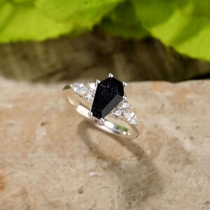 May include: A silver ring with a black coffin-shaped gemstone and smaller clear gemstones around it.