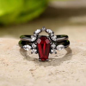 May include: Black ring set with a red coffin-shaped gemstone and white cubic zirconia accents.