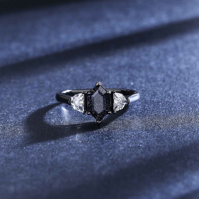 May include: A black ring with a large, dark, octagonal-shaped gemstone surrounded by two smaller, clear, triangular-shaped gemstones.