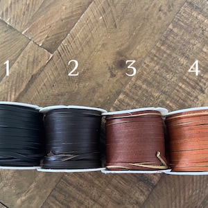 Four spools of leather lace in different colors labeled 1 to 4: black, dark brown, brown, and camel, arranged in a row on a rustic wooden surface. Ideal for crafting, jewelry making, or leatherwork projects.