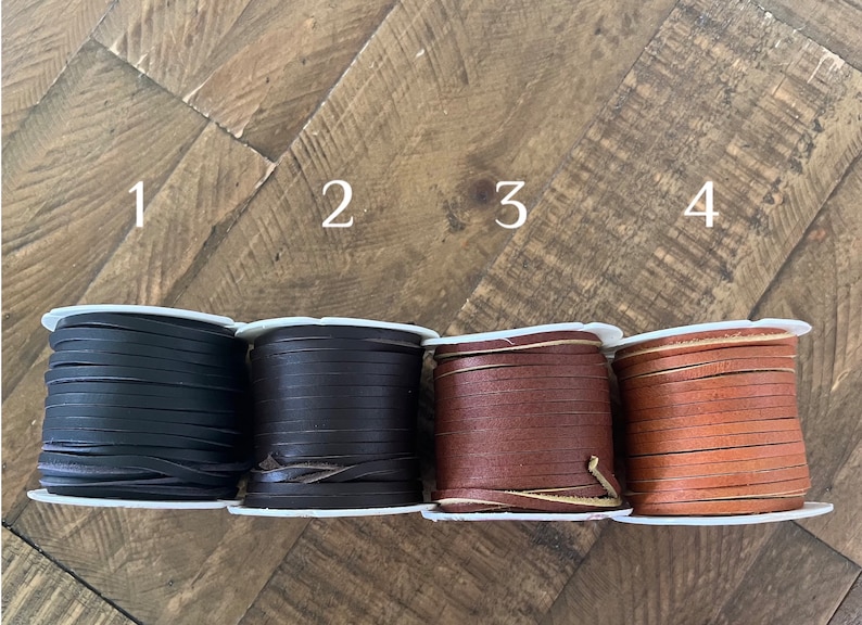 Four spools of leather lace in different colors labeled 1 to 4: black, dark brown, brown, and camel, arranged in a row on a rustic wooden surface. Ideal for crafting, jewelry making, or leatherwork projects.