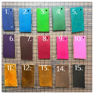 Fifteen leather color swatches labeled 1 to 15 in various shades: blue, turquoise, green, teal, purple, brown, tan, red, pink, black, yellow, and gold. Displayed on a cutting mat, ideal for custom leathercraft or DIY projects