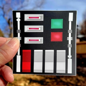 May include: A black and white control panel sticker with red, green, and white buttons. The sticker has a Star Wars theme.