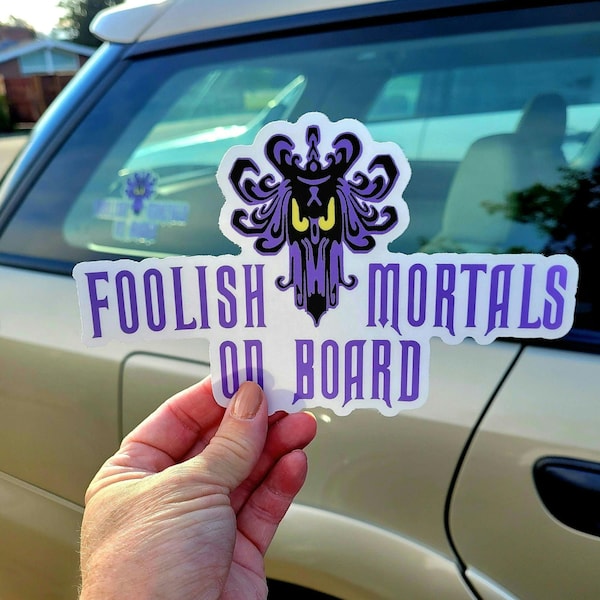 May include: A white sticker with purple text that reads "Foolish Mortals On Board". A purple and black illustration of a ghost with a crown is centred above the text.