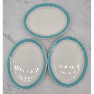 May include: Three oval-shaped ceramic plates with a white center and a light blue rim.