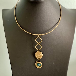 Puede incluir: Un collar gargantilla de oro con un colgante con un diseño en espiral y una piedra preciosa azul.