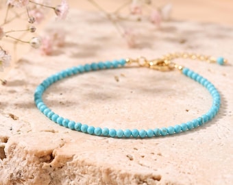 May include: A delicate bracelet featuring small, round, bright turquoise beads strung on a thin gold-toned chain. The bracelet includes a gold-toned lobster claw clasp and an adjustable extender chain with a single turquoise bead at the end.