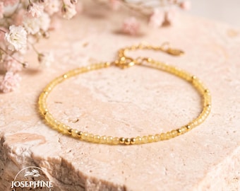 May include: A delicate bracelet featuring small, faceted yellow beads interspersed with tiny gold-toned metal spheres. The jewelry piece includes a gold-toned chain extension with a clasp and a small circular logo tag reading JOSEPHINE.