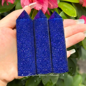 May include: Three blue glitter crystal points with a pointed top and a flat base. The points are arranged in a row and are held in a hand.