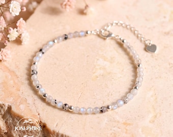 May include: A delicate bracelet featuring small, round, iridescent labradorite beads interspersed with tiny silver-toned metal beads. The bracelet includes a silver-toned chain extender with a small heart-shaped charm at the end.