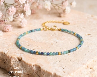 May include: A delicate bracelet featuring small, faceted blue and green gemstone beads interspersed with tiny gold-toned metal spacers. The jewelry piece includes a gold-toned chain extender with a circular clasp and a small round charm.