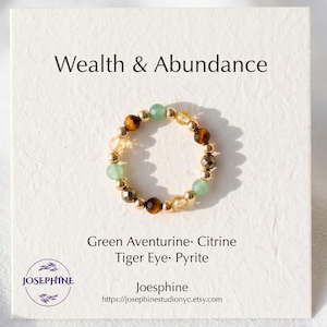 May include: A beaded ring featuring alternating green aventurine, citrine, tiger eye, and pyrite beads on a display card labeled Wealth & Abundance. The card lists the stone names and includes the brand name Josephine and a website URL.