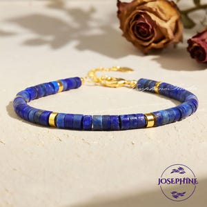 May include: A blue beaded bracelet with gold accents. The bracelet features small, flat, blue beads and gold-colored metal spacers. The clasp and connecting chain are also gold. The brand name "Josephine" is in a circle at the bottom.