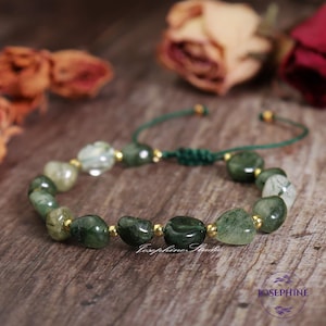 May include: Green and clear gemstone bracelet with gold accents and a green cord closure. The bracelet is made of natural stones and is a beautiful and unique piece of jewelry.