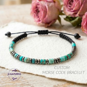 May include: A custom Morse code bracelet with turquoise and gray beads strung on a black cord. The bracelet is displayed on a white surface with pink roses in the background. The text "CUSTOM MORSE CODE BRACELET" is visible.