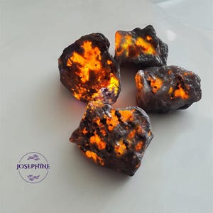 May include: Four rough, dark gray, and black stones with orange and yellow inclusions. The stones are illuminated from within, creating a glowing effect.