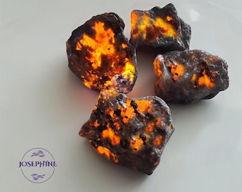 May include: Four rough, dark grey and black stones with orange and yellow inclusions. The stones are illuminated from within, creating a glowing effect.