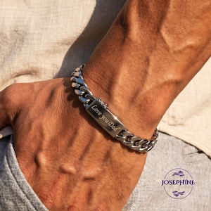 Könnte beinhalten: Ein silberfarbenes Panzerkettenarmband mit einer rechteckigen Platte mit der Gravur "Love you Dad". Das Armband wird am Handgelenk getragen. Das Armband hat einen klobigen Stil mit einem sicheren Verschluss.