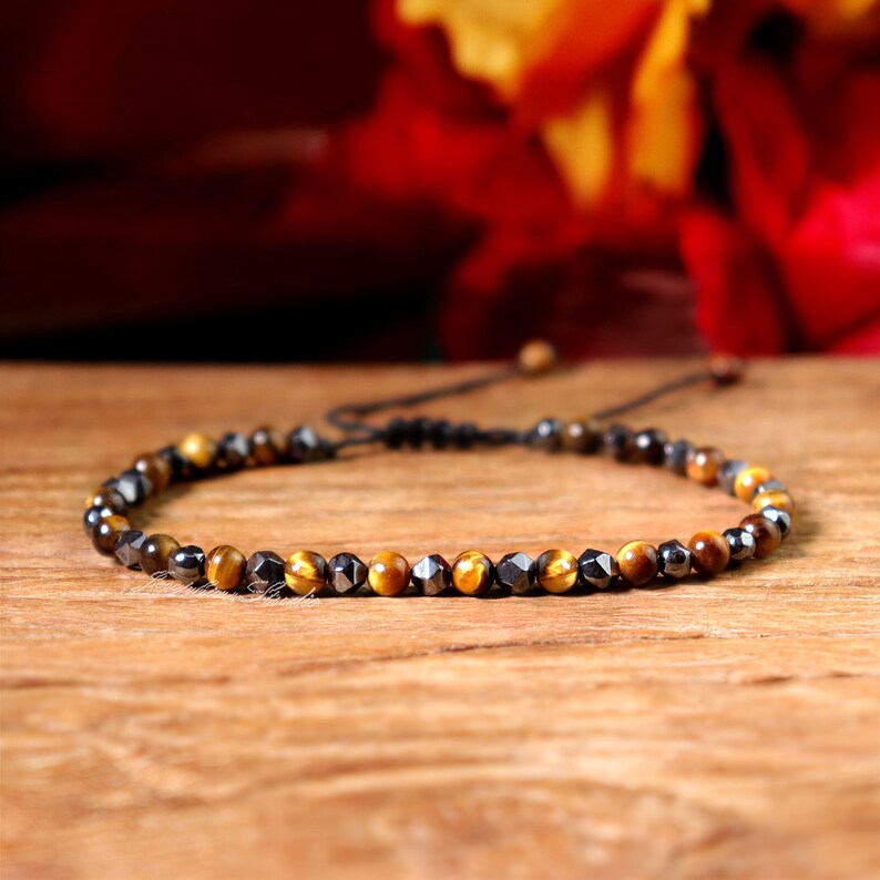 May include: A beaded bracelet with alternating black and gold beads. The bracelet is made with a black cord and has a sliding knot for adjusting the size.