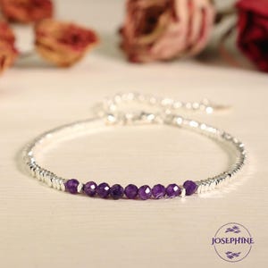 May include: A silver bracelet with a row of purple amethyst beads. The bracelet is made of small, square-shaped silver beads.