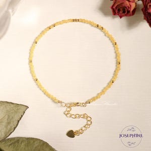 May include: A delicate bracelet featuring small, faceted pale yellow beads interspersed with tiny gold-toned metal spheres. The piece includes a gold-toned chain extender with a small heart-shaped charm at the end and a lobster clasp closure.