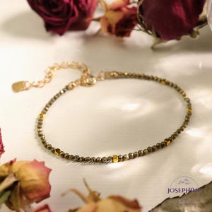 May include: A delicate gold bracelet with a chain closure and small, dark green beads interspersed with gold accents.