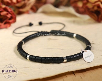 Puede incluir: Pulsera de cuentas negras con detalles plateados y un dije plateado con la palabra "JOSEPHINE" grabada.