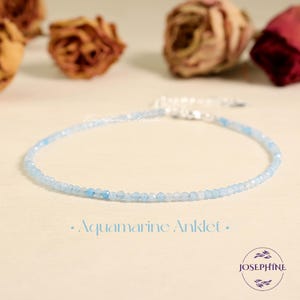 May include: A delicate aquamarine anklet with small, light blue beads strung together. The anklet is displayed on a light-colored surface with dried roses in the background. The text "Aquamarine Anklet" is below the anklet.