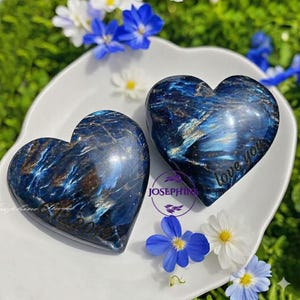 May include: Two heart-shaped, polished stones with a swirling blue and brown pattern. One heart has the text "love you" etched on it. The other heart has the text "Josephine Star 12.2019". The hearts are on a white plate, surrounded by blue and white flowers.