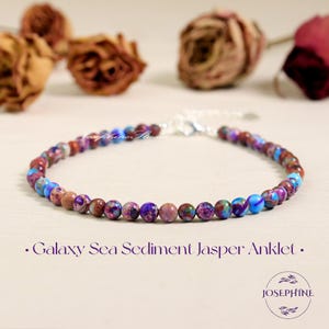 以下が含まれることがあります： 紫、青、茶色のGalaxy Sea Sediment Jasperビーズで作られたアンクレット。ビーズは留め金付きのシルバーチェーンに通されています。テキスト:「Galaxy Sea Sediment Jasper Anklet」。ジュエリーアイテム。