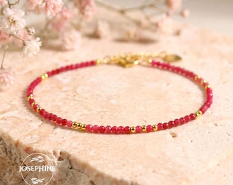 May include: A delicate bracelet featuring small, faceted deep pink beads interspersed with tiny, polished gold-tone metal spheres. The jewelry piece includes a gold-tone metal clasp and a small circular tag with the text JOSEPHINE.