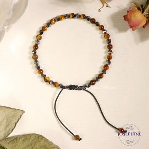 May include: A brown and black beaded bracelet with a black cord and adjustable clasp. The bracelet is made with tiger's eye and hematite beads.