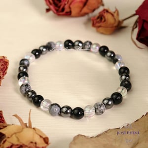 May include: A black, gray, and iridescent beaded bracelet. The bracelet is made with round beads of various sizes and colors.