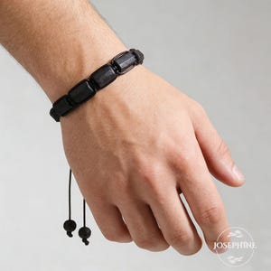 May include: Black bracelet featuring rectangular beads strung together with black cord. The bracelet has a sliding knot closure for adjustable sizing. The beads appear to be made of a dark, possibly natural material.