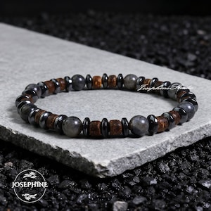 May include: A beaded bracelet featuring a mix of dark gray, brown, and black beads. The bracelet includes round, cylindrical, and disc-shaped beads. The brand name "Josephine Studio" is visible on the bracelet.