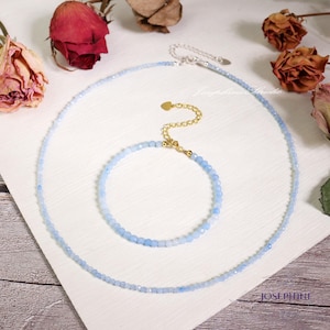 Könnte beinhalten: Ein Set aus zwei zarten Halsketten aus hellblauen Edelsteinperlen. Die längere Halskette ist eine zarte Kette mit einem kleinen Herzanhänger. Die kürzere Halskette ist ein Armband mit einem Verschluss.